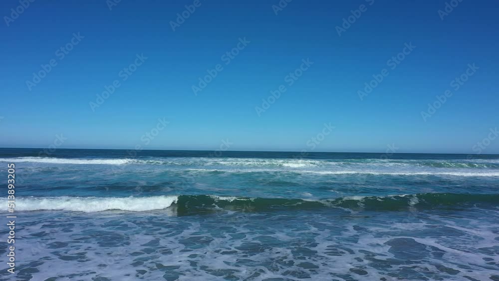 Aerial shot over waves slowly crashing with nothing but blue skies on the horizon. Aerial shot over waves slowly crashing with nothing but blue skies on the horizon.