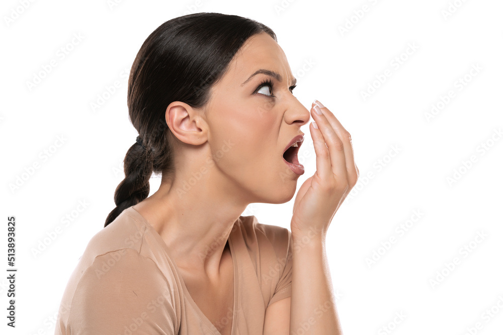 Profile of a young frowning woman checks her breath with her palm on a white background Profile of a young frowning woman checks her breath with her palm on a white background
