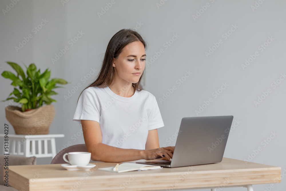 beautiful European woman is at home in the living room resting or working on a laptop. A stylish young adult woman with long hair poses and looks at the camera. a day off or vacation for recreation