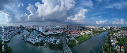 Aerial panorama of Ho Chi Minh City with canal, city skyline and traffic bridge in afternoon light and dramatic sky