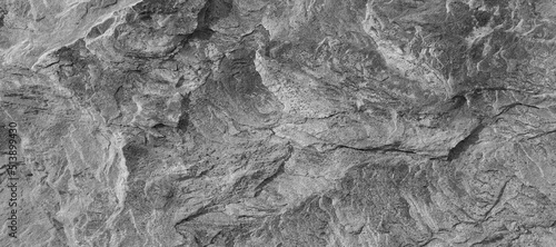 Dark Aged Shabby Cliff Face And Divided By Huge Cracks And Layers. Coarse, Rough Gray Stone Or Rock Texture Of Mountains, Background And Copy Space For Text On Theme Geology And Mountaineering.