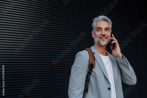 Successful happy businessman waiting in city street, calling on mobile phone, commuting concept.