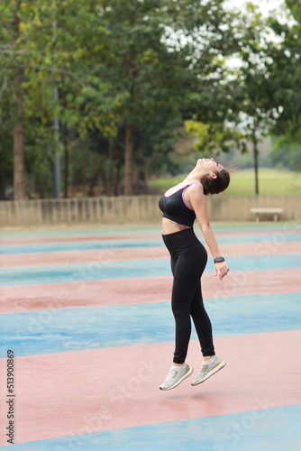 Athletic young asian woman in sportswear standing and doing cardio interval training outdoor for morning exercise. Active and healthy girl jumping over with green tree background. Sport concept