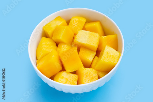 Yellow mango cube slices in white bowl on blue background.