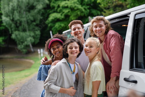 Multiracial young friends travelling together by car, looking at camera and smiling - summer vacation, holidays, travel, road trip and people concept.