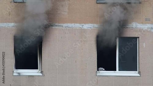 Gray thick smoke billows from two windows of an apartment building. Extinguishing a fire in a high-rise building. Fire in the apartment. A firefighter shines a lantern in a dark window. photo