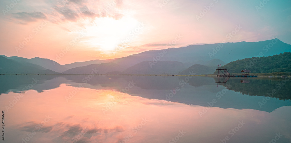 Panorama scenic of mountain lake with perfect reflection at sunrise. beautiful mountain range landscape with pink pastel sky with hills on background and reflected in water. Nature lake landscape
