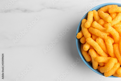 Bowl of tasty cheesy corn puffs on white marble table, top view. Space for text