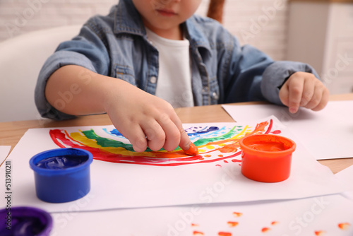 Little child painting with finger at wooden table indoors, closeup