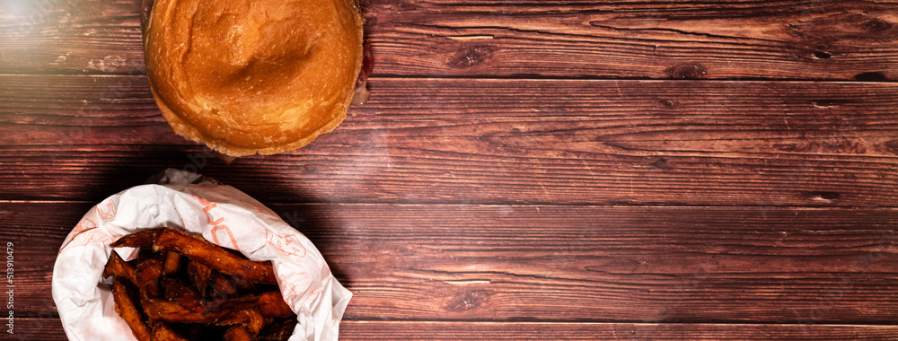 Top view of a hamburger with french fries on a dark wood table. Beef burger. Horizontal banner with space for text. Top view of a hamburger with french fries on a dark wood table. Beef burger. Horizontal banner with space for text.