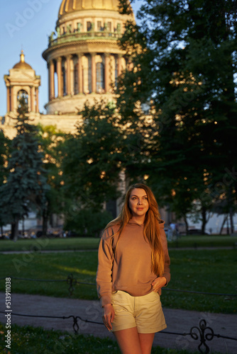 a young woman in the sunbeams stands on the lawn near a high cathedral in a european city. tourism, city walks