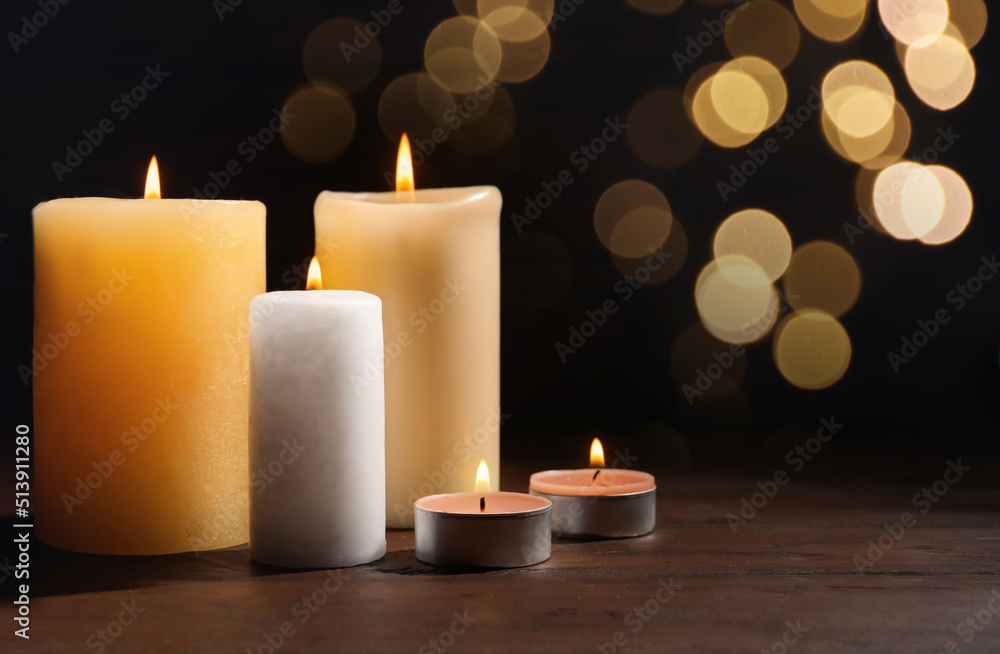 Different wax candles burning on table against dark background with blurred lights. Bokeh effect