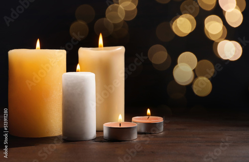 Different wax candles burning on table against dark background with blurred lights. Bokeh effect