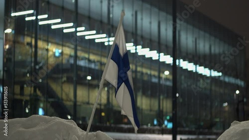 Small Finland flag in snow bank at night outside illuminated building photo