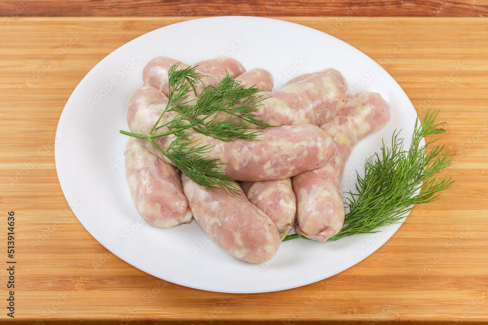 Raw short thick chicken sausages with fresh dill on dish Raw short thick chicken sausages with fresh dill on dish