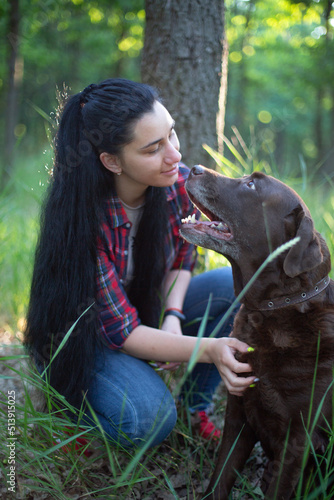 a young caucasian woman in a red plaid shirt plays with an old labrador dog in a green park