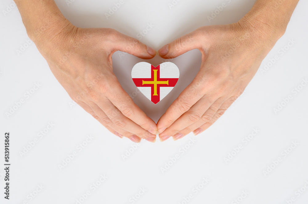 Obraz premium National flag of Guernsey in the shape of a heart in female hands on a light background.