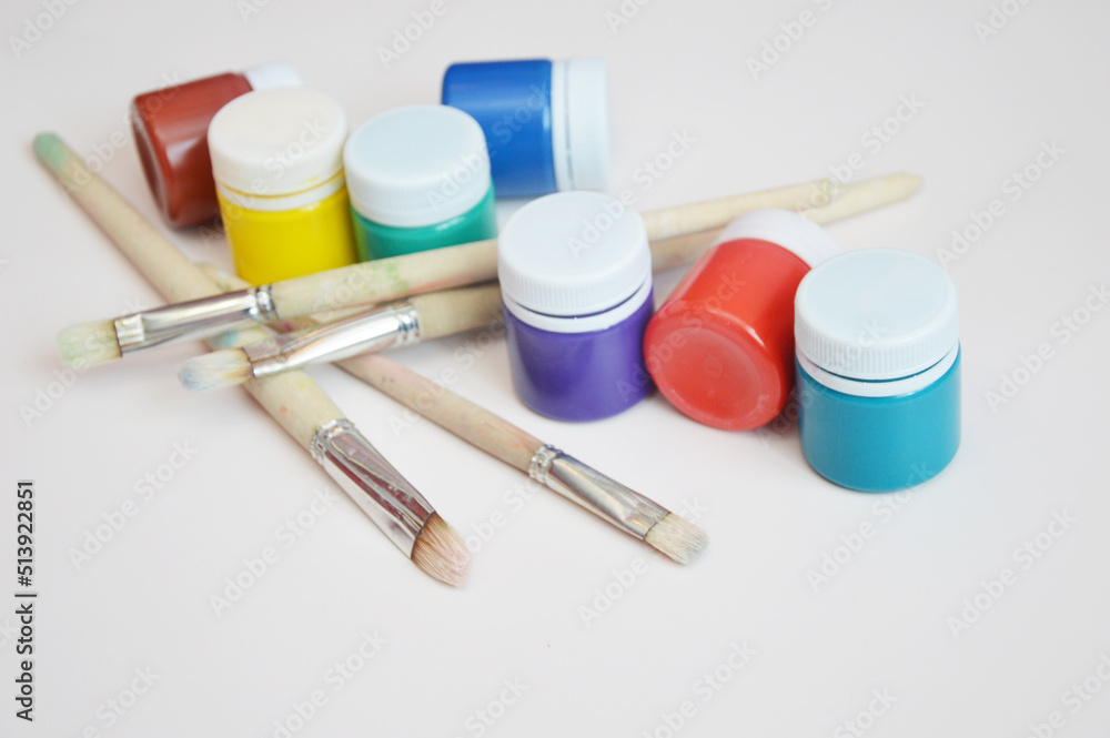 Gouache paints, closed jars of different colors with artistic brushes, on a light background. Workplace of an illustrator, artist. Gouache paints, closed jars of different colors with artistic brushes, on a light background. Workplace of an illustrator, artist.