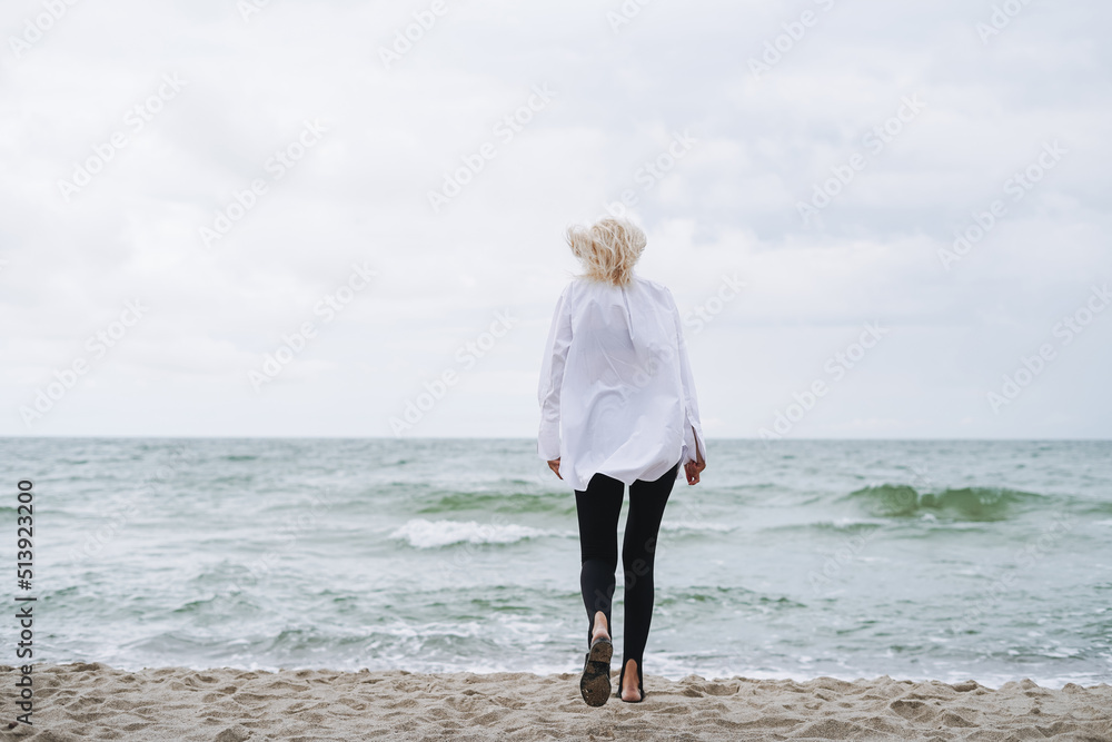 Portrait of Elegant blonde woman in white shirt on sand beach at storm sea at windy weater Portrait of Elegant blonde woman in white shirt on sand beach at storm sea at windy weater