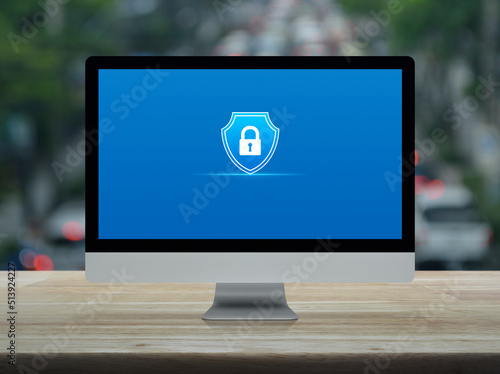 Padlock with shield flat icon on desktop modern computer monitor screen on wooden table over blur of rush hour with cars and road in city, Technology security insurance online concept