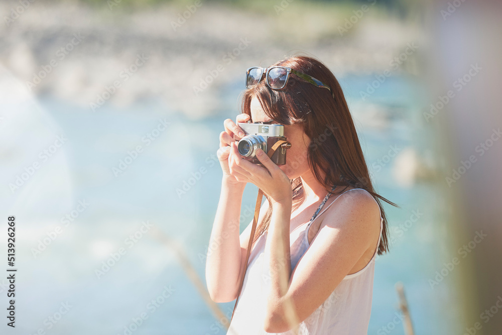 young woman taking photos of nature on her digital camera during a holiday. Young woman on a holiday adventure using her digital camera to take photos of the natural scenery by a river