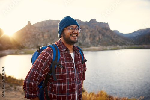 A young adult backpacker smiles at the lake view with sunset in the mountains 