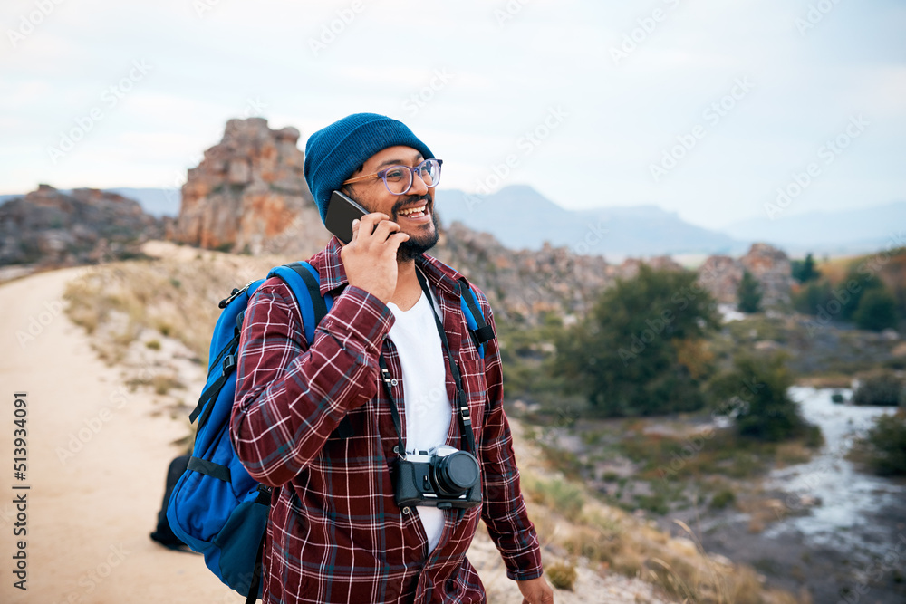 Naklejka premium A young backpacker laughs on a call in the mountains while hiking in autumn