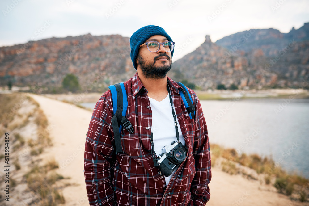 A backpacker stares out into the mountains while hiking with camera next to lake
