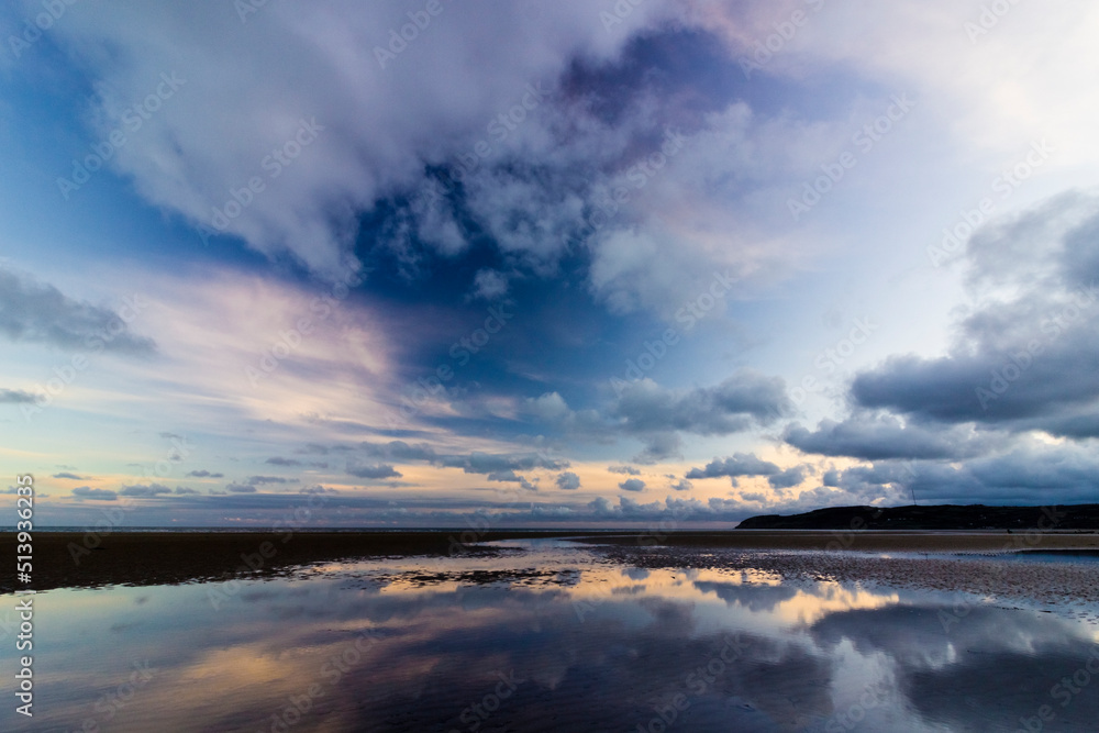 Dramatic twilight cloudscape and skyscape reflection on the water pooled surface of Red Wharf Bay, Isle of Anglesey, North Wales