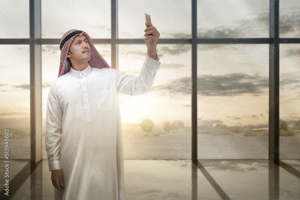 Arab man wearing keffiyeh looking at mobile phone inside the room Arab man wearing keffiyeh looking at mobile phone inside the room