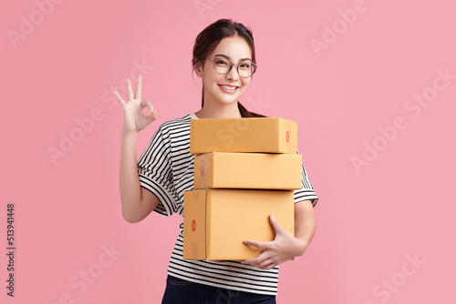 Beautiful Young Asian woman holding parcel box isolated on pink background, Delivery courier and shipping service concept. © kitthanes