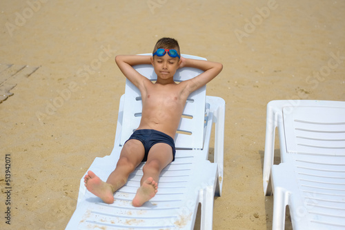 Young guy in swimming glasses is sunbathing on a sunbed on the sea beach.