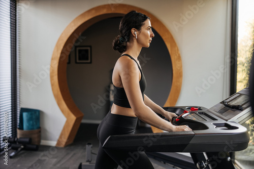 Calm caucasian young brunette woman runs on cardio machine in gym. Girl wears black sportswear. Healthy lifestyle, keep fit concept.