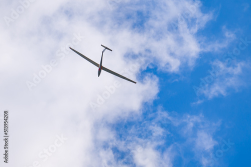 Sailplane flying under white clouds in blue sky