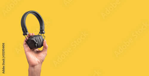 Banner with hand holding wireless headphones on yellow background. Listening to music, taking phone calls. Copy space. High quality photo