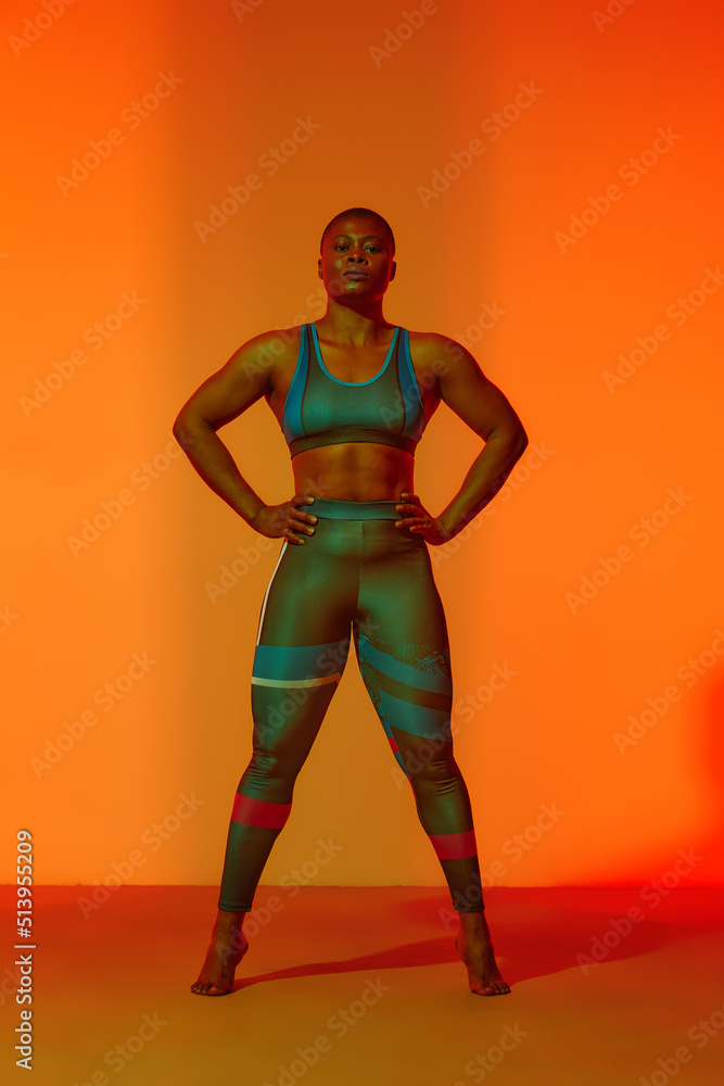 Happy african american woman wearing sportive clothes showing plus size hips. Body positive concept. Yellow light on background