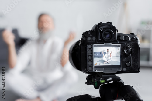 selective focus of digital camera near senior yoga coach meditating in easy pose.