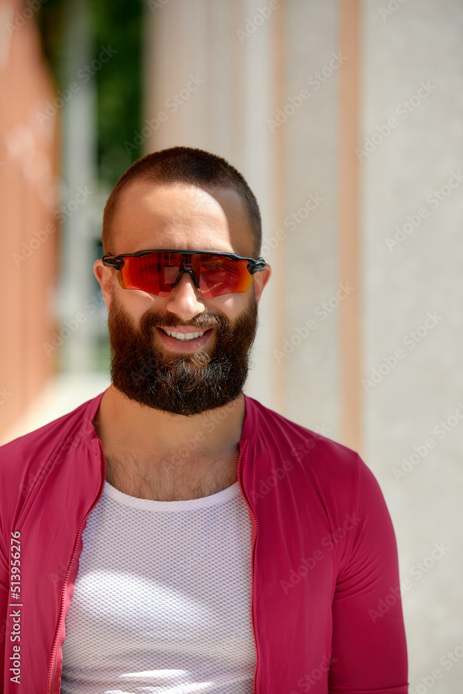 Close up shot of happy attractive young European man with beard wearing glasses and pink sportswear looking at camera during evening ride in park on weekend. Close up shot of happy attractive young European man with beard wearing glasses and pink sportswear looking at camera during evening ride in park on weekend.