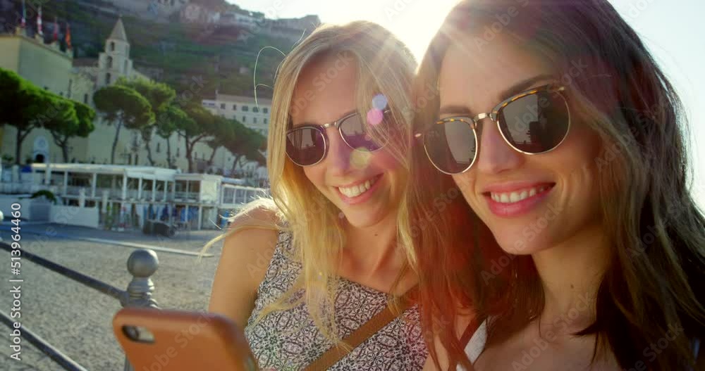 Two women using a smartphone while on vacation. Happy friends looking at a smartphone screen on holiday Two women using a smartphone while on vacation. Happy friends looking at a smartphone screen on holiday