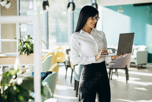 Attractive business woman in formal wear standing in office and holding laptop