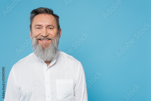 happy bearded man in white shirt looking at camera isolated on blue.