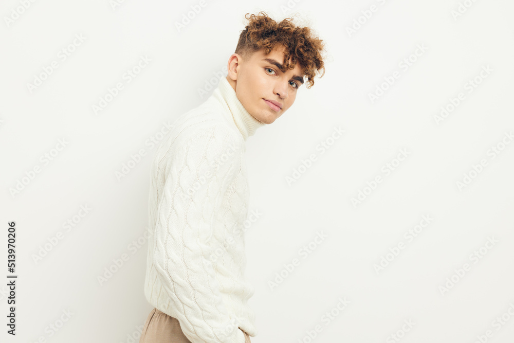 a close horizontal photo of a handsome, attractive man with curly hair, standing in a white knitted sweater on a light background, smiling pleasantly at the camera. a close horizontal photo of a handsome, attractive man with curly hair, standing in a white knitted sweater on a light background, smiling pleasantly at the camera.