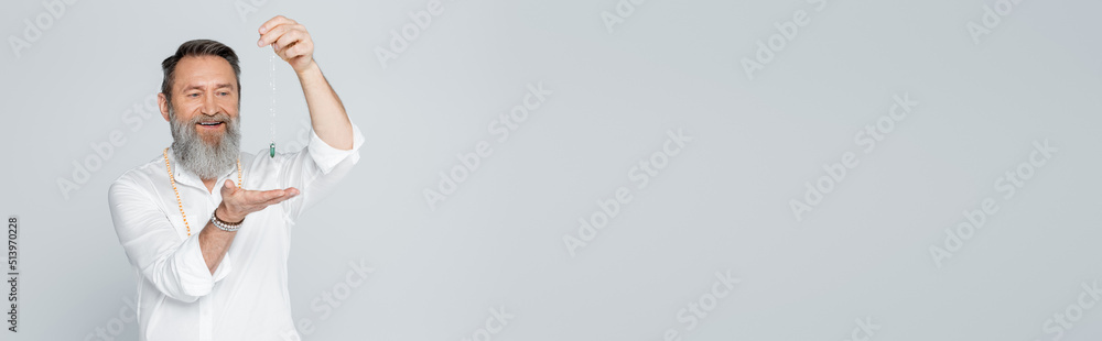 smiling guru man in white shirt holding dowsing pendulum isolated on grey, banner. smiling guru man in white shirt holding dowsing pendulum isolated on grey, banner.