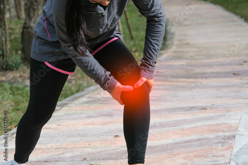 Female runner touches her knee in pain while jogging in a park. Runner sport knee injury.