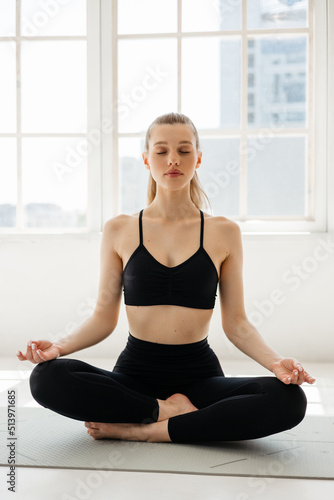 Sports girl meditating on a fitness mat against the background of a window