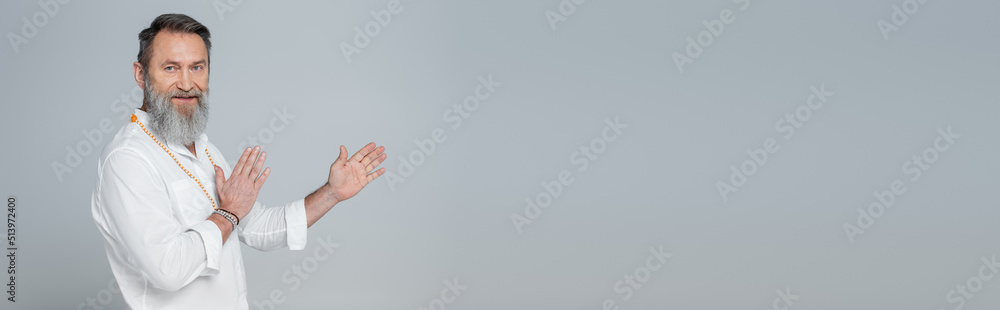 bearded master guru in white shirt looking at camera and pointing with hands isolated on grey, banner. bearded master guru in white shirt looking at camera and pointing with hands isolated on grey, banner.