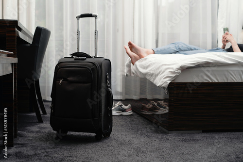 woman taking off footwear in a hotel room on the bed. Tourist relaxing on hotel room after travelling with suitcase. Female having rest after long trip with language Dark silhouette 
