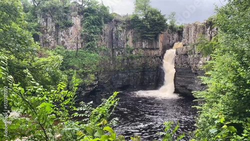 High Force Waterfall through some green trees in a cloudy day. Teesdale, North-East England UK, Still shot. photo