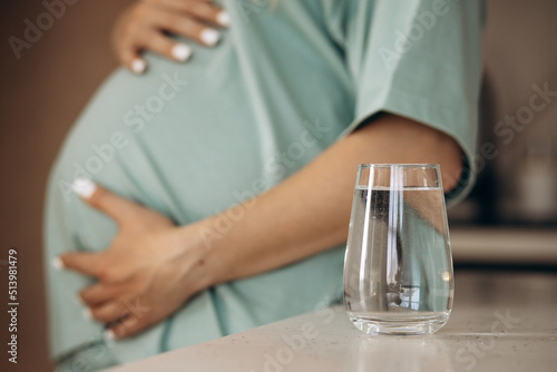 Pregnant woman hugging her belly by the glass full of water