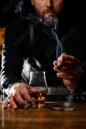 smoking cigar in the hand of a male bartender and a glass of cognac